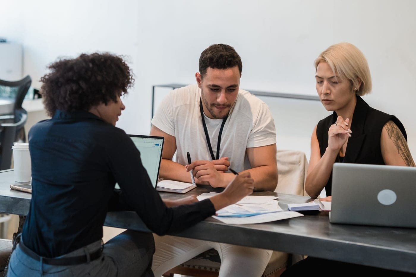 Tre persone lavorano insieme su documenti e portatili intorno a un tavolo.